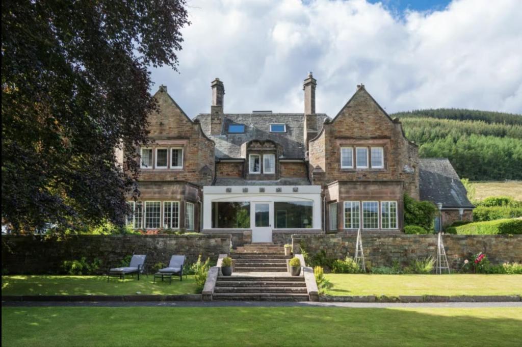 an old stone house with two chairs on the lawn at Windlestraw Guesthouse in Walkerburn