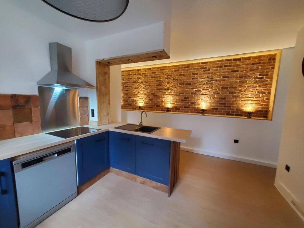 a kitchen with blue cabinets and a brick wall at Refuge Éclatant Paray 4 couchages in Paray-le-Monial