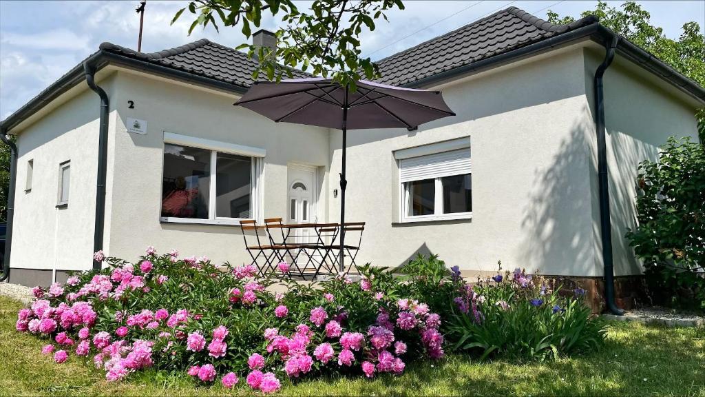 a house with a table and an umbrella and flowers at Alma2 Vendégház in Révfülöp