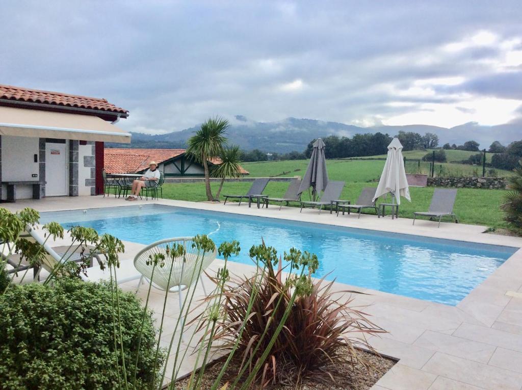 a pool with chairs and umbrellas next to a house at Hotel Restaurant Pecoitz in Saint-Jean-Pied-de-Port