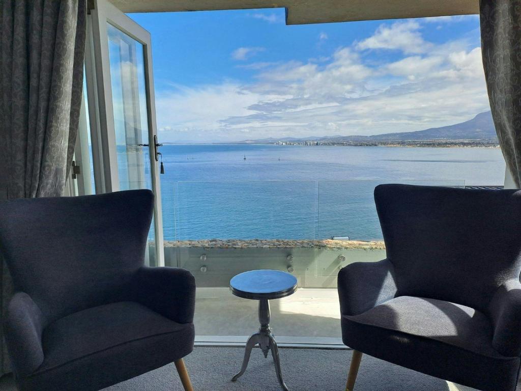 a room with two chairs and a view of the water at Boutique Inn - Azure in Gordonʼs Bay