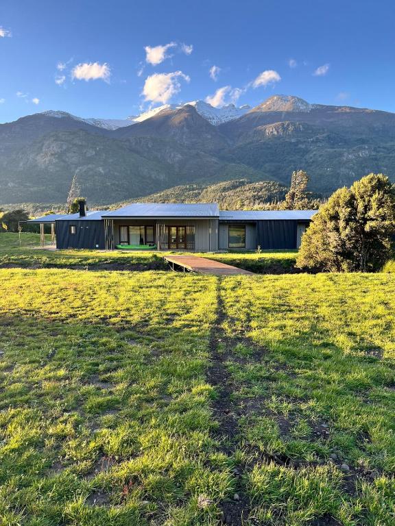 a house in a field with mountains in the background at Límite Sur Lodge in Trevelín