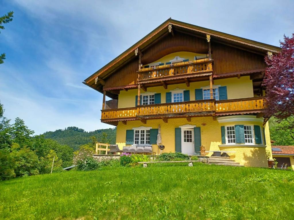 a large yellow house with a balcony on a hill at Ferienwohnung 'Bergidylle' - Zu Fuß auf die Loipe und den Berg, nur wenige Minuten ins Skigebiet in Bayrischzell