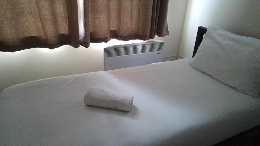 Una cama blanca con una toalla enrollada. en City View Hotel Stratford en Londres
