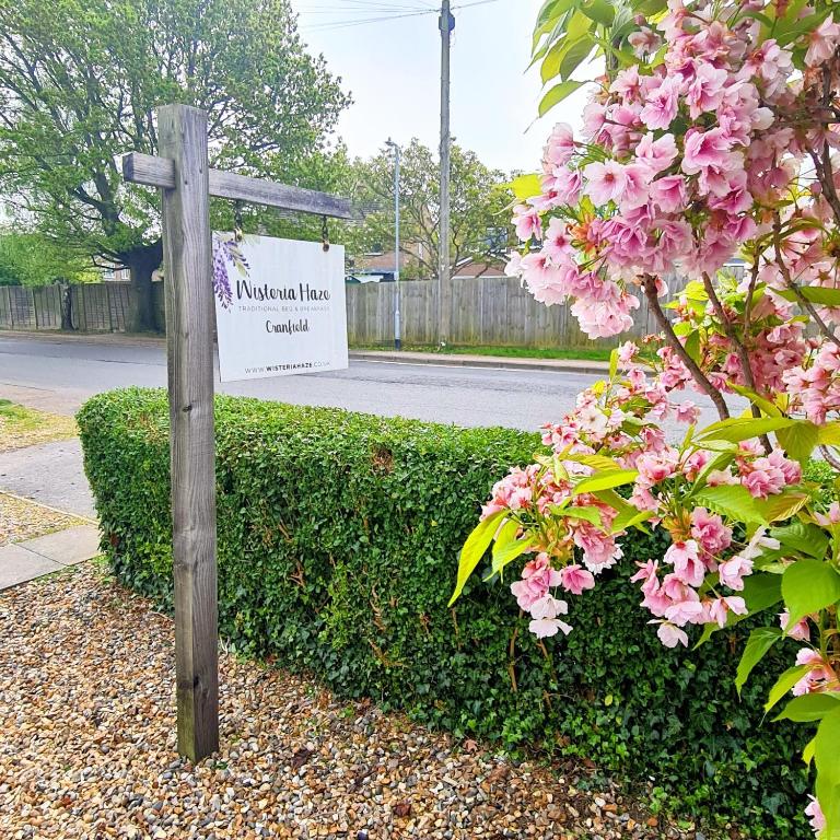 a sign in front of a bush with pink flowers at Wisteria Haze in Cranfield