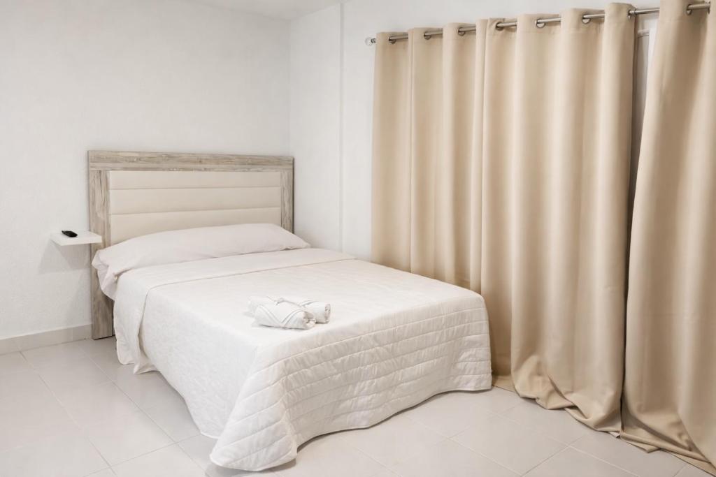 a bedroom with a bed with white sheets and curtains at Alicante Beach Hostel in Alicante