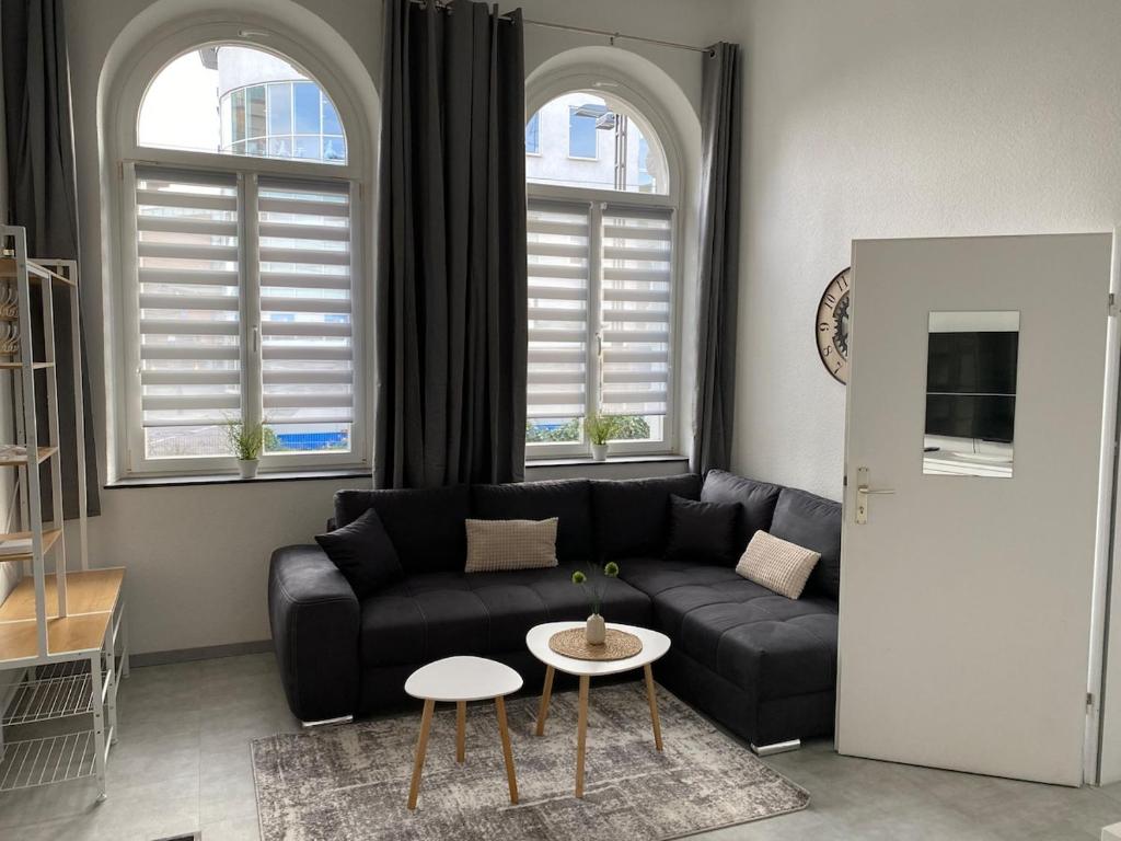 a living room with a black couch and two windows at Ferienwohnung in Solingen Innenstadt in Solingen