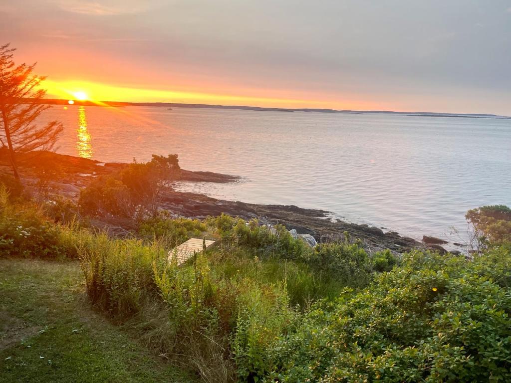 a sunset over a body of water with the sun setting at Barnacle - quiet family Maine waterfront getaway in Orrs Island