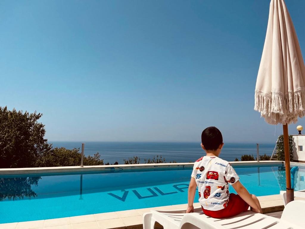 a young boy sitting on a chair next to a swimming pool at Rozana Rooms in Ulcinj