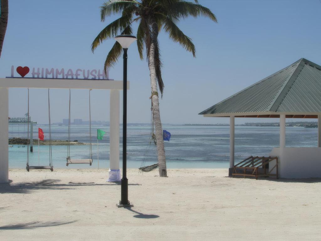 a palm tree and a sign on the beach at Gk Eleven in Himmafushi