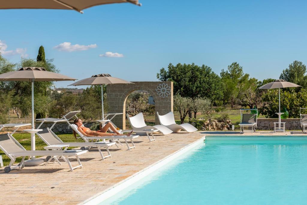 a woman sitting in lounge chairs next to a swimming pool at Agriturismo Residenza Gemma in Porto Cesareo