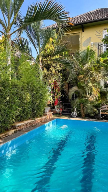 a blue swimming pool in front of a house with palm trees at Hide Out Lake Villa Uganda in Bwerenga