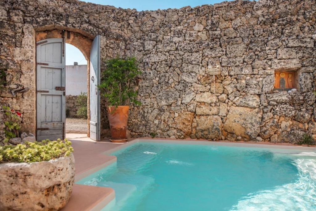 a swimming pool in front of a stone wall at Masseria De Li Travaj - Rive del Salento in Patù