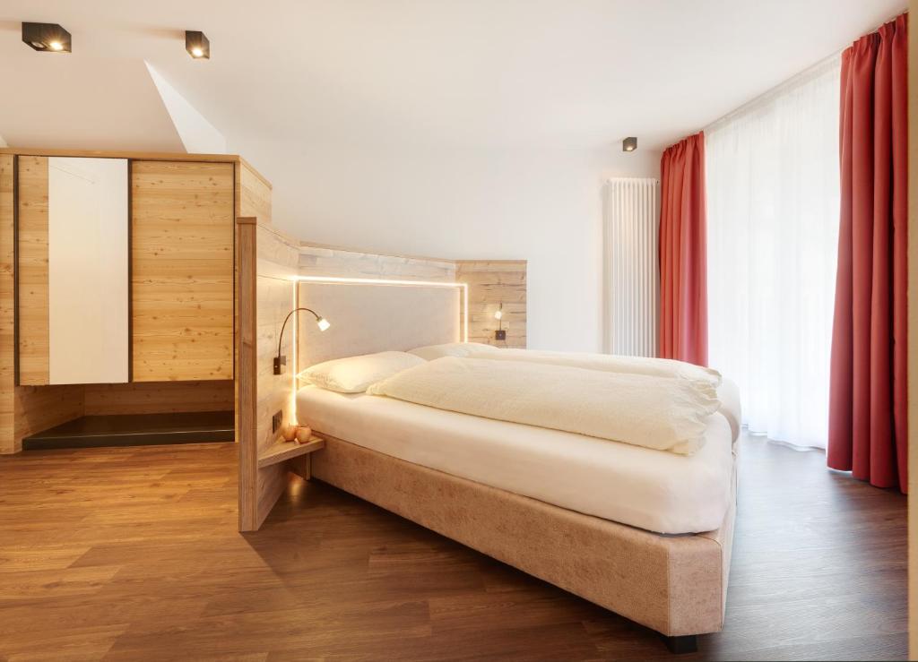 a bedroom with a large white bed and red curtains at Hotel Al Cervo in Tesero