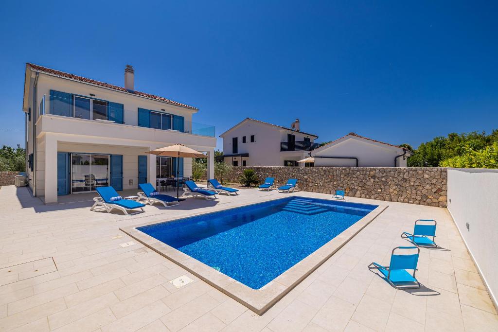 a swimming pool with blue chairs and a house at Holiday house DAN with private pool in Kras