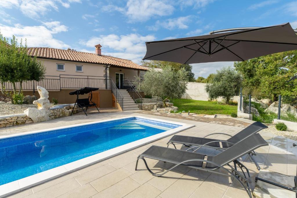 a swimming pool with an umbrella and two chairs and a table at House Cerovac in Nedeščina