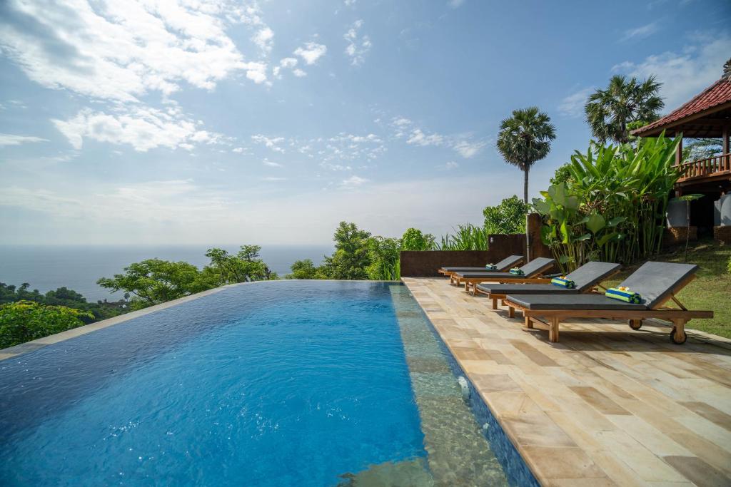 a swimming pool with chaise lounge chairs next to a resort at Kubu Diar by Manara in Seraya