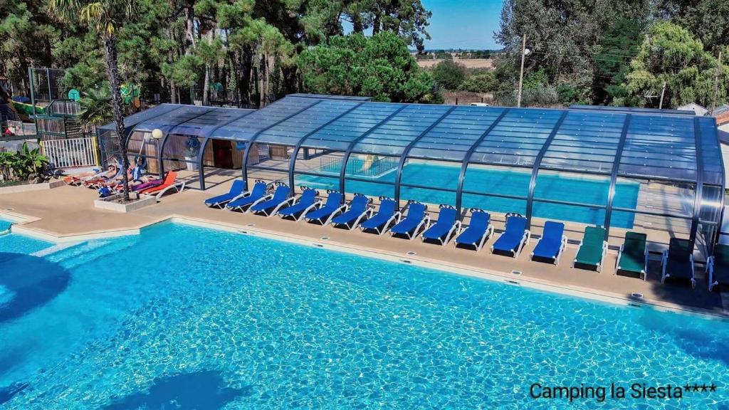 a swimming pool with chairs and a building at Camping La Siesta - Maeva in L'Aiguillon-la-Presqu'île