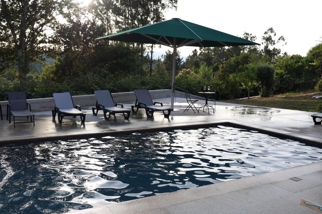 a pool with chairs and an umbrella and a table at Qt Refúgio de Rubiães Villa 1-2 Paredes de Coura in Paredes de Coura