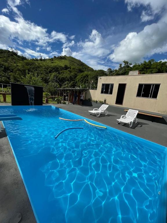 a large blue swimming pool with two chairs and a building at Suites Clarinda in Capitólio