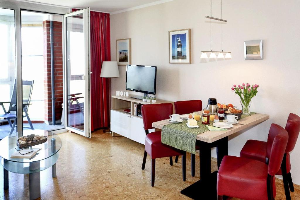 a living room with a dining room table and red chairs at Haus Horizont I HZ21 in Cuxhaven