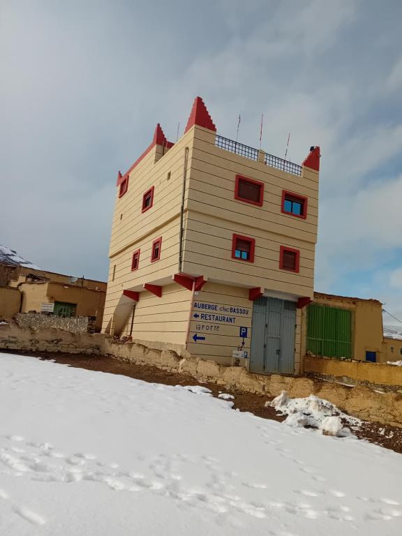 a wooden building with red windows in the snow at Auberge Chez Bassou Agoudal in Agoudal