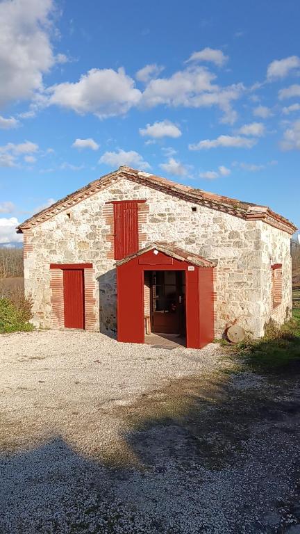 a stone barn with red doors on a field at Gîte FABEL HAUT in Durfort