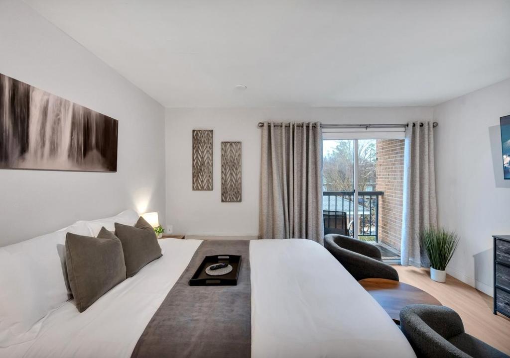 a white bedroom with a large bed and chairs at Modern Midtown Studio and Private Balcony in Raleigh