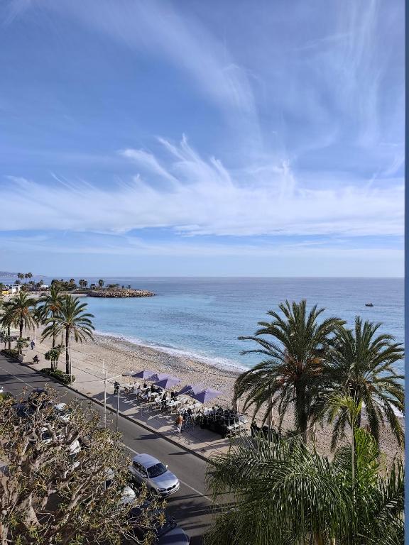 a beach with palm trees and chairs and the ocean at Victoria Plaza in Menton