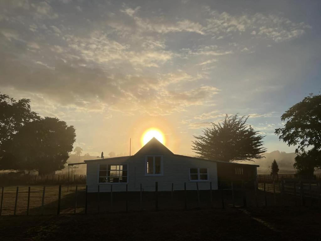 a white house with the sun setting behind it at Destination Cliff Top - Cottage and Homestead in Ohingaiti