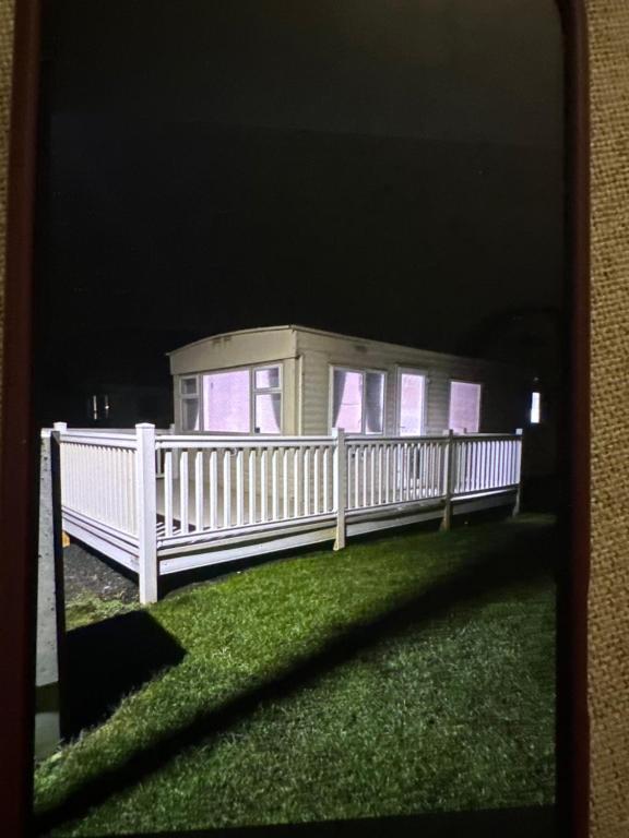 a house with a white fence on the grass at Sandylands caravan park in Stevenston