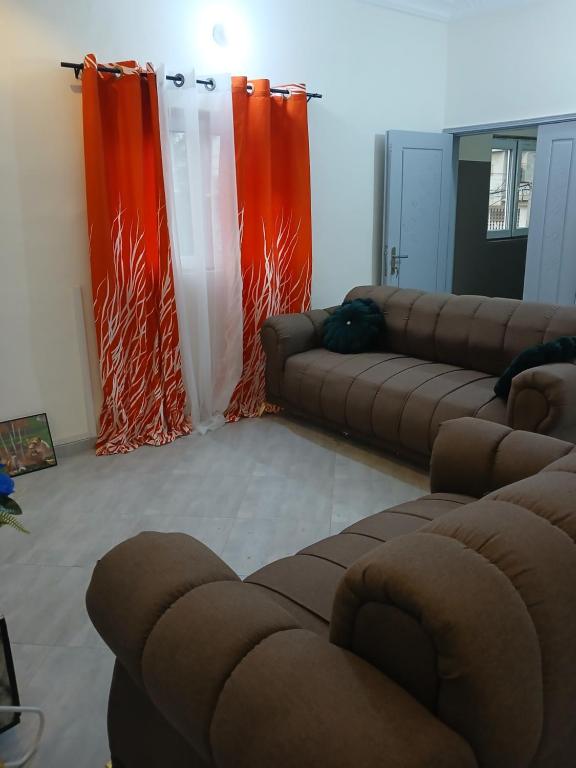 a living room with two couches and orange curtains at Christal house in Abomey-Calavi