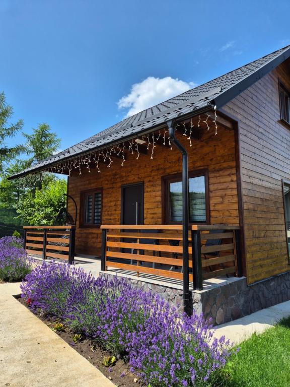 a log cabin with purple flowers in front of it at Casuta Sofiei in Vîrfu Dealului