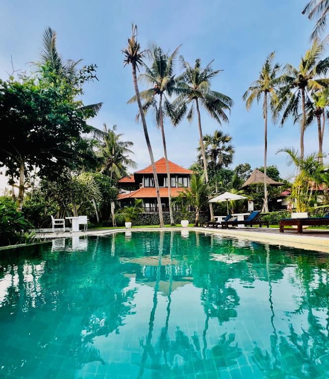 a swimming pool in front of a house with palm trees at The Palms - Seraya Shores Retreat Bali in Seraya