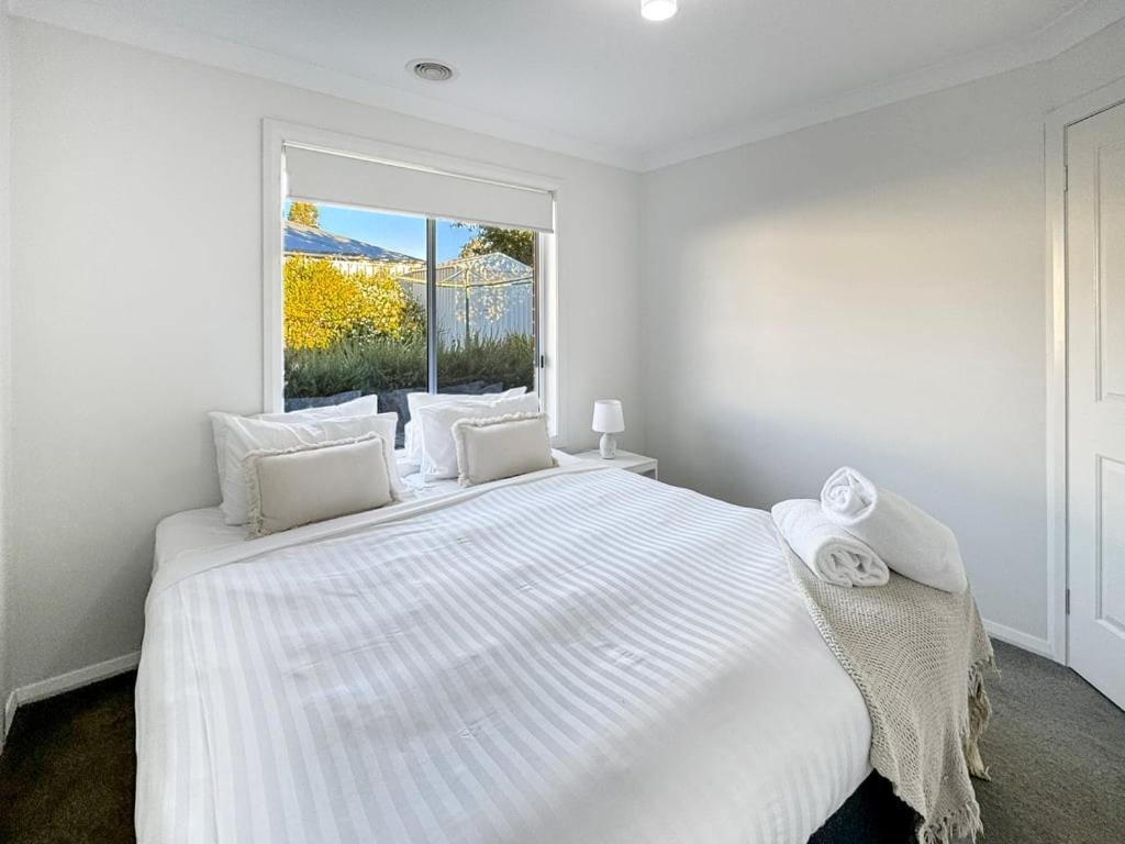 a white bedroom with a large white bed and a window at St Pauls Home in North Wagga