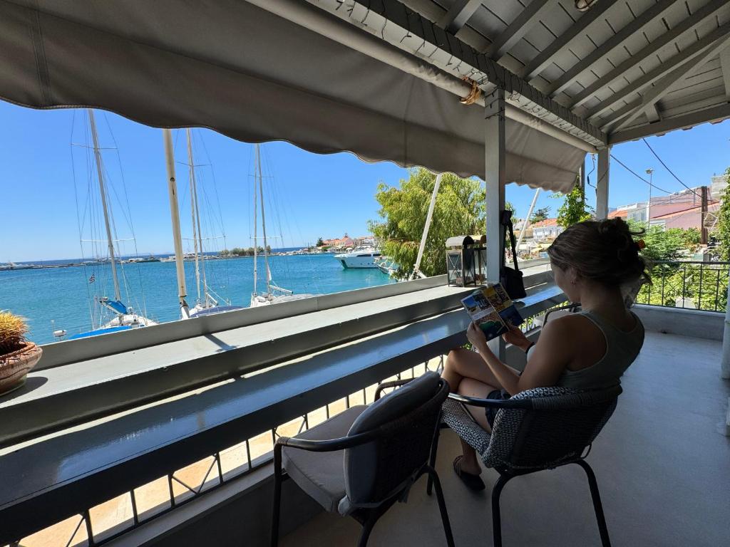 a woman sitting in a chair reading a book near a window at Pythagorion Harbour Residence in Pythagoreio