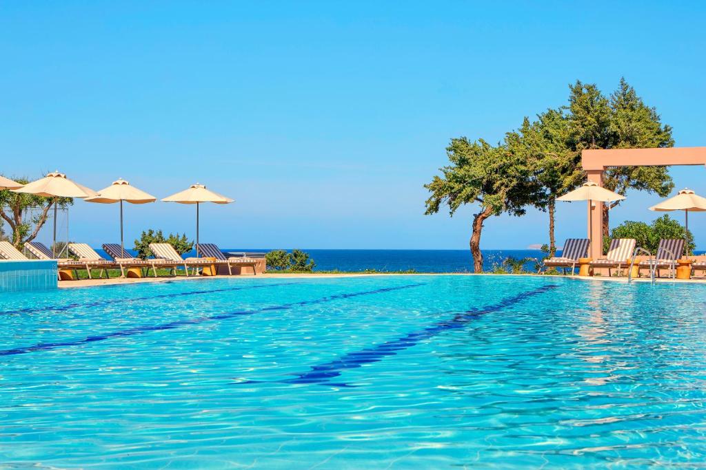 a swimming pool with umbrellas and the ocean at Zeus Kos Beach in Mastihari