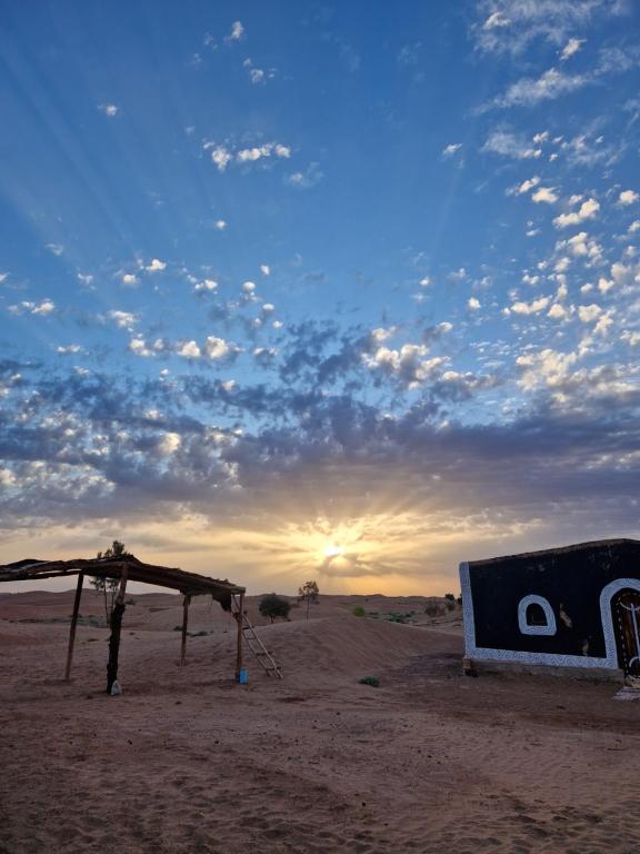 a structure in the middle of a desert with a sunset at Sahara Authentic Berber Camp in Mhamid