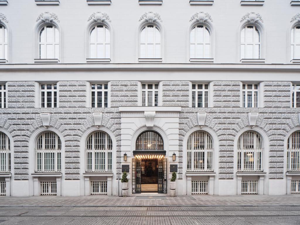 White classical facade with arched windows, decorative stone frieze and double-glass entrance with brass lanterns at Hotel Capital in Zagreb
