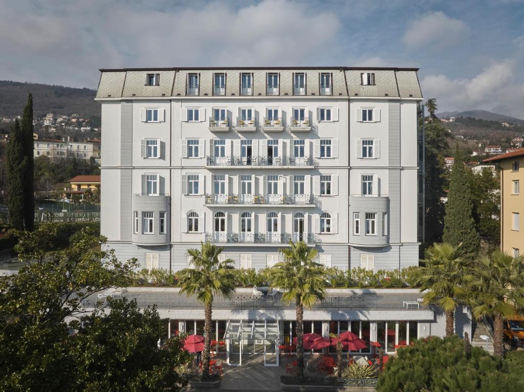 a large white building with palm trees in front of it at Hostel Link in Lovran