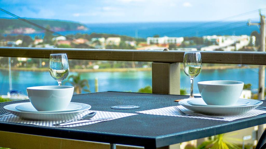 a table with two glasses of wine on a balcony at Hydra Holiday Units in Merimbula