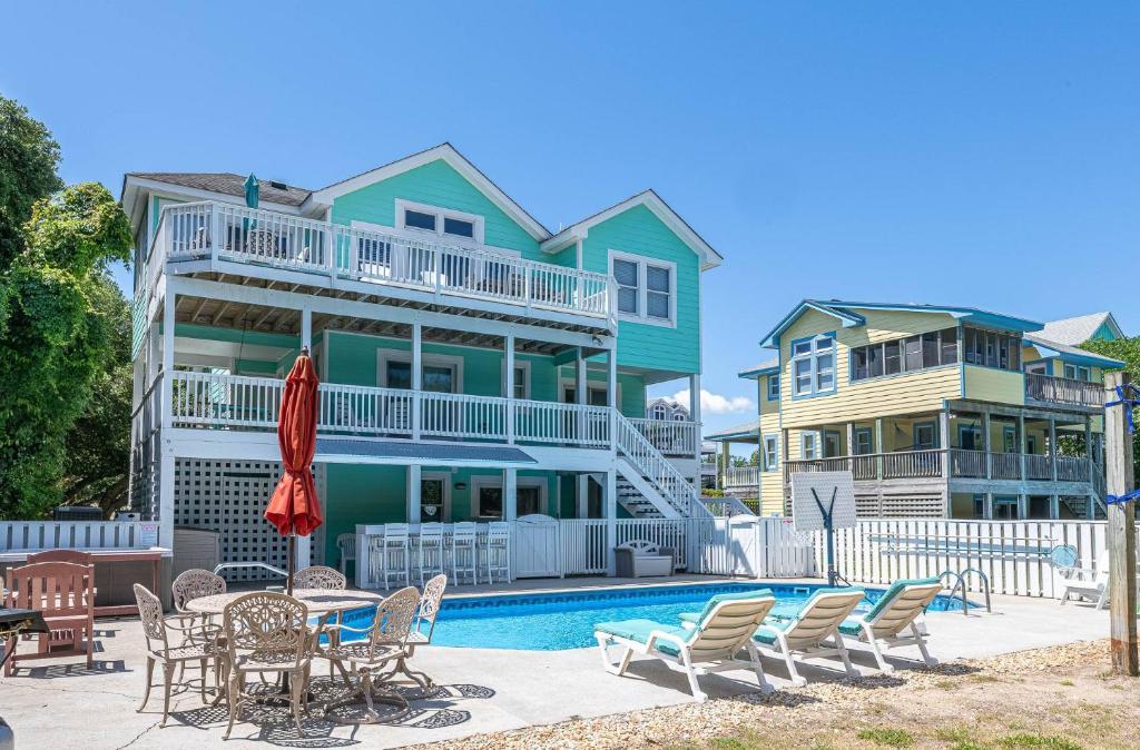 a house with a swimming pool and chairs and a table at Family Tradition - Duck Landing, Oceanside, 130 Yds to Beach, Pool, Hot Tub, Tiki Bar in Duck