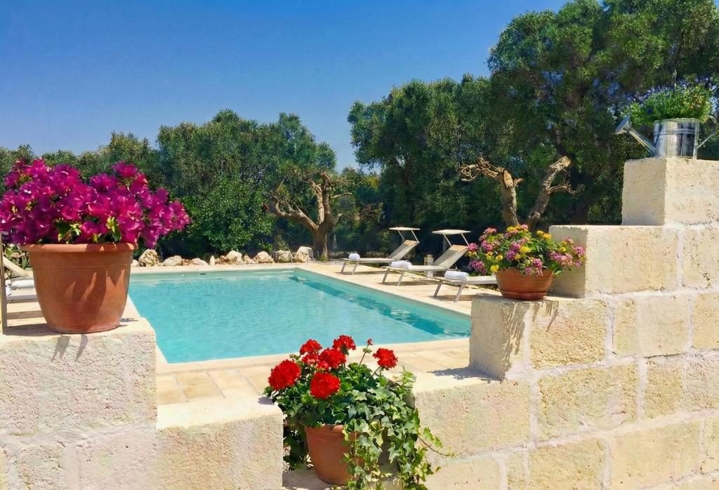 a pool with flowers in pots next to a wall at Dimora Antonella - Ostuni 4 seasons - Splendid Villa Depandance with Private Swimming Pool in Ostuni