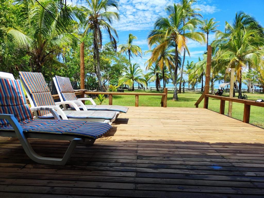three lounge chairs on a wooden deck with palm trees at Cabaña con Deck Frente al Mar para 8 personas in Moñitos