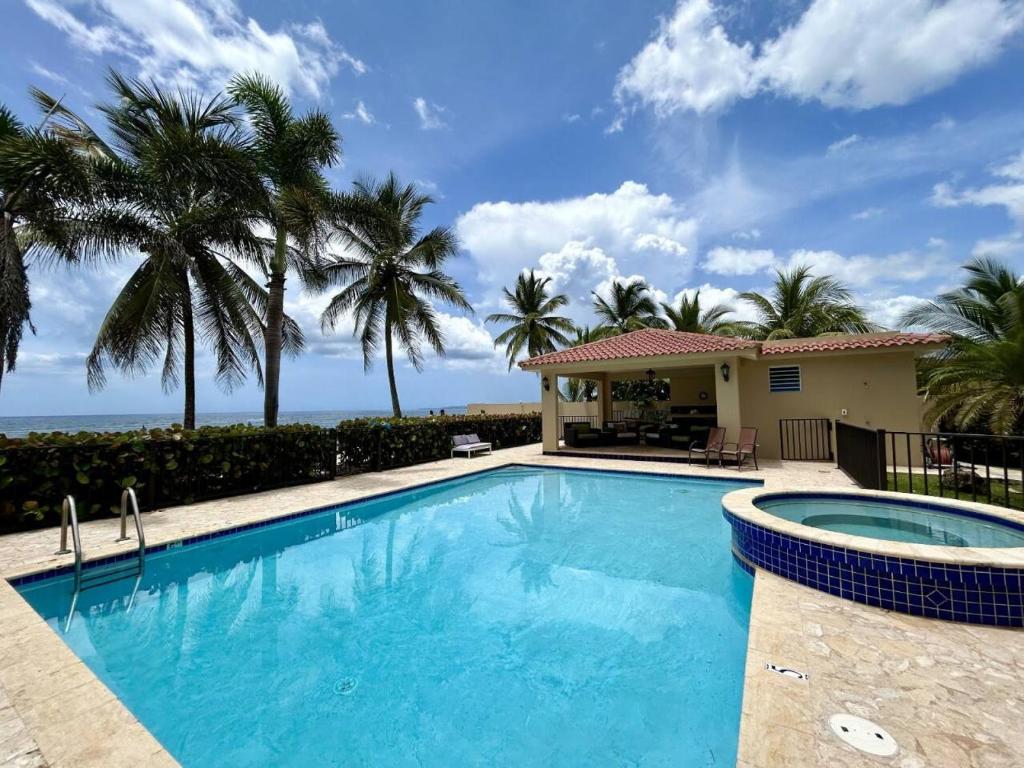 a swimming pool with palm trees and a house at Ocean Vibes near Rincón Beachfront Access Condo in Matias