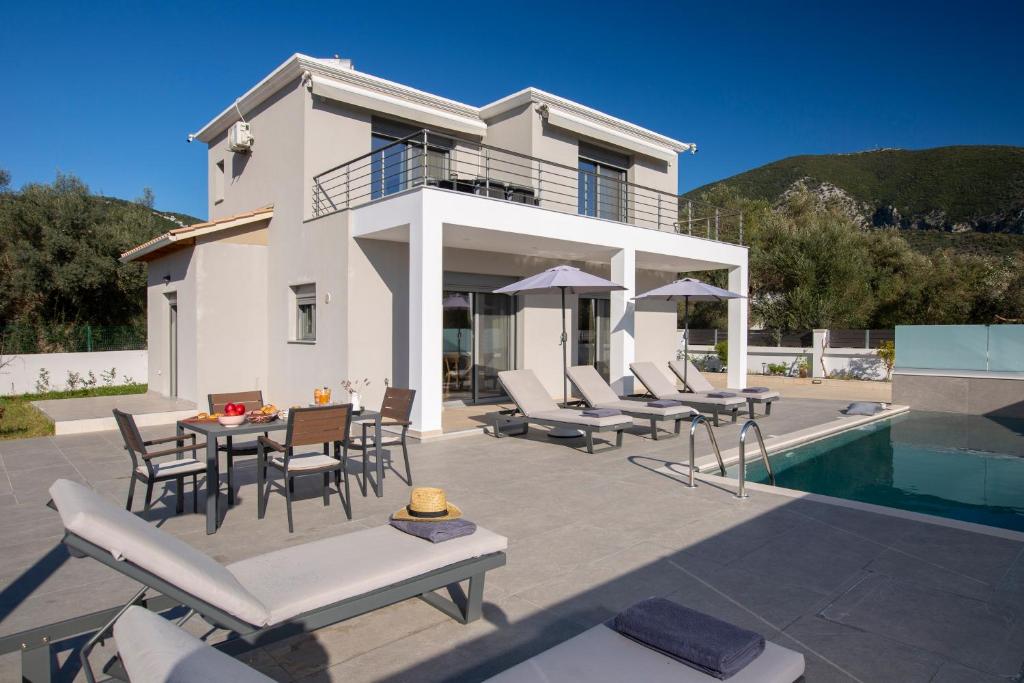a white house with chairs and a table and a pool at Valora Villa in Nydri