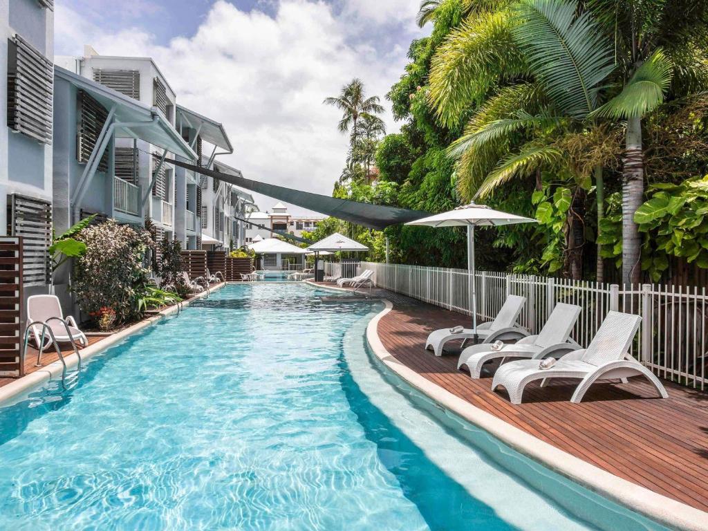 a swimming pool with chairs and umbrellas next to a building at Mantra Aqueous on Port in Port Douglas