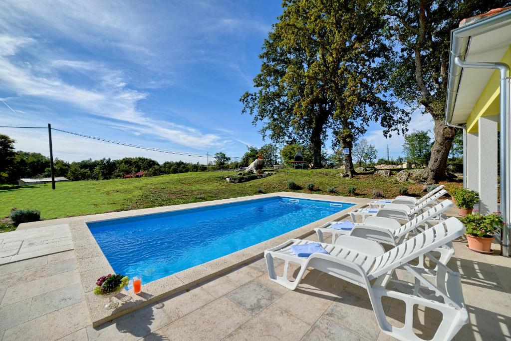 a swimming pool with white chairs next to a house at Cozy villa Paradiso with pool immersed in the greenery in Marčana
