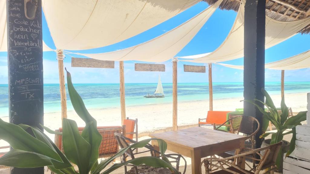 a table and chairs on a beach with a sailboat in the ocean at Garden Beach Bungalows Jambiani in Jambiani