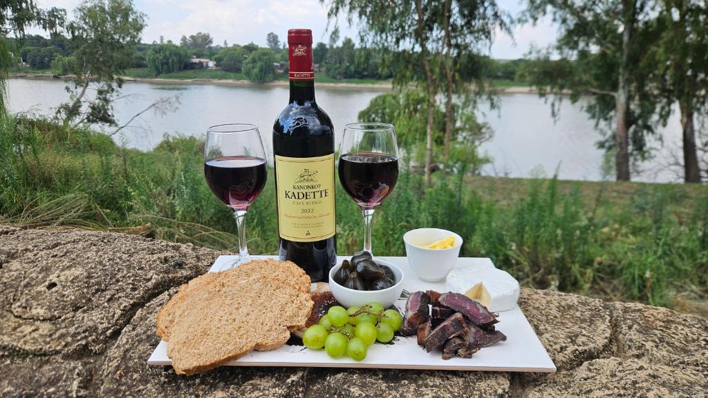 a bottle of wine and a plate of food and wine glasses at Grobler's Haven On Vaal - Barrage in Tumahole